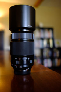 Fuji 55-200 on a wood table with a bookshelf blurred in the background